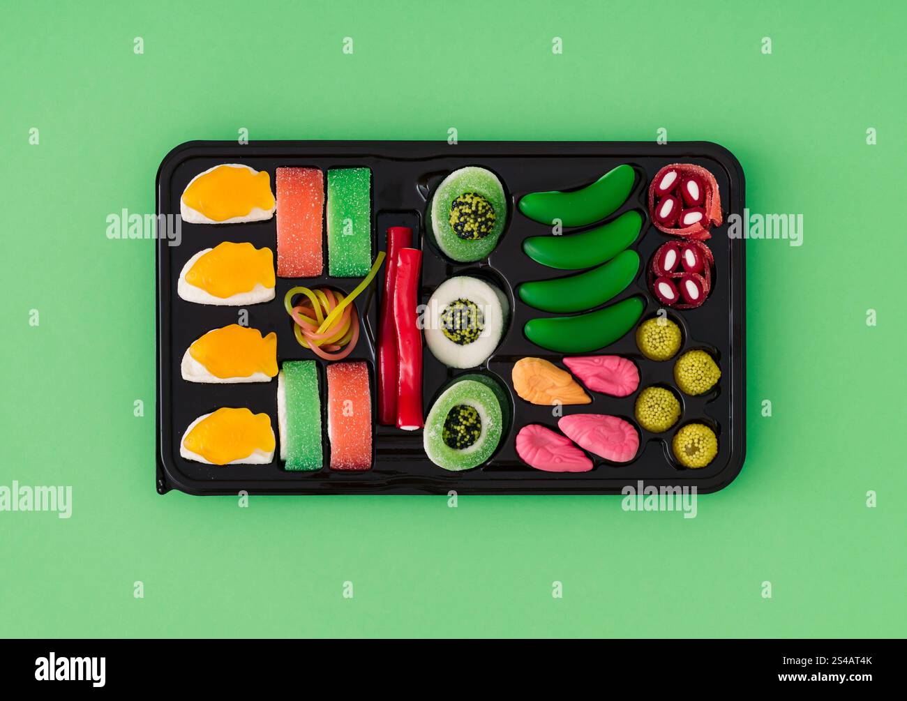 Morbido mix di caramelle su sfondo verde pastello. Concetto minimalista di sushi caramelle. Un'idea di sushi surreale alla moda. Caramelle gommose estetiche. Posizione piatta, vista superiore. Foto Stock