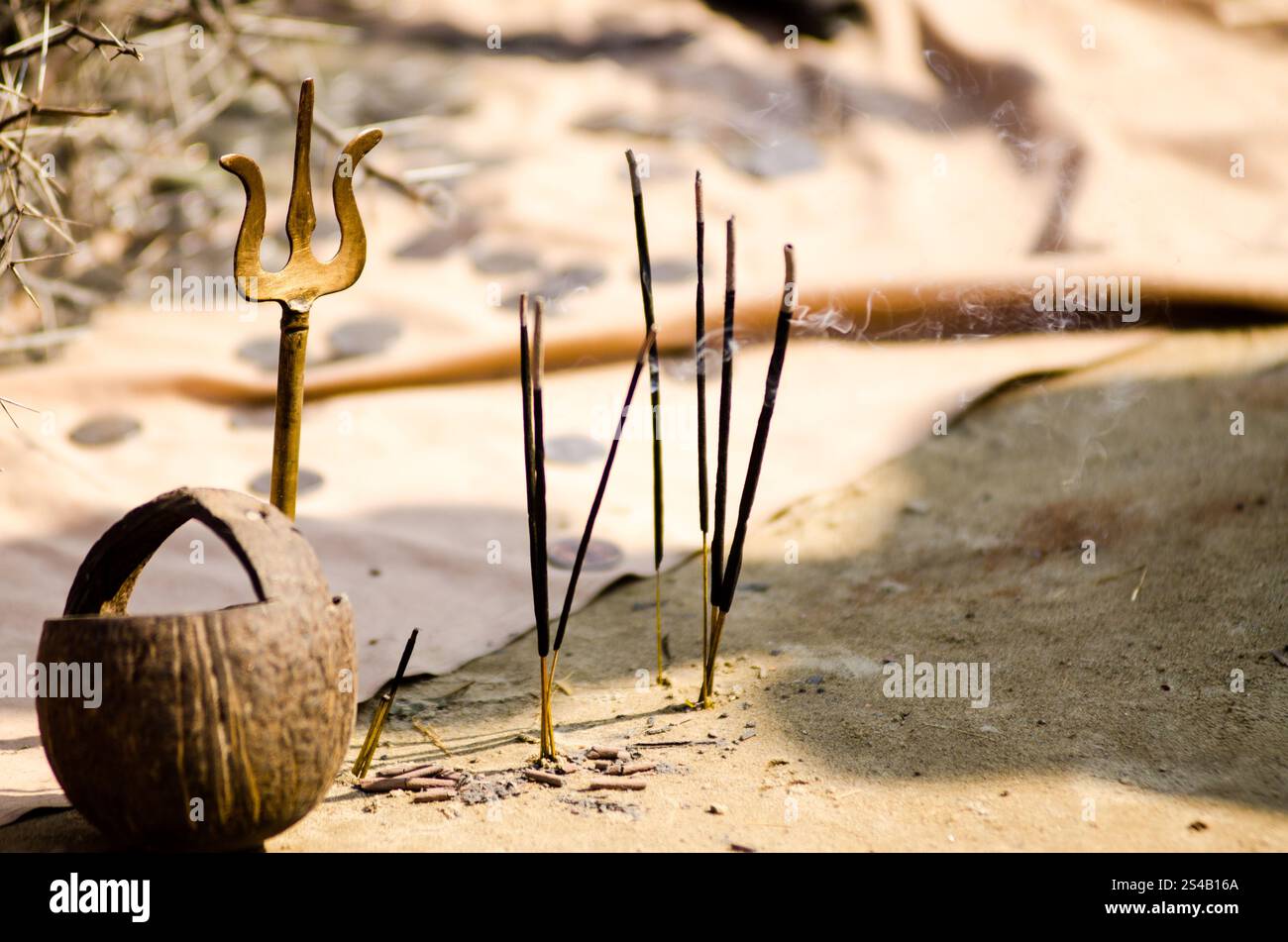 Oggetti rituali, tra cui bastoncini di incenso, un tridente e una ciotola cerimoniale collocata su un terreno terroso durante un raduno spirituale all'aperto Foto Stock