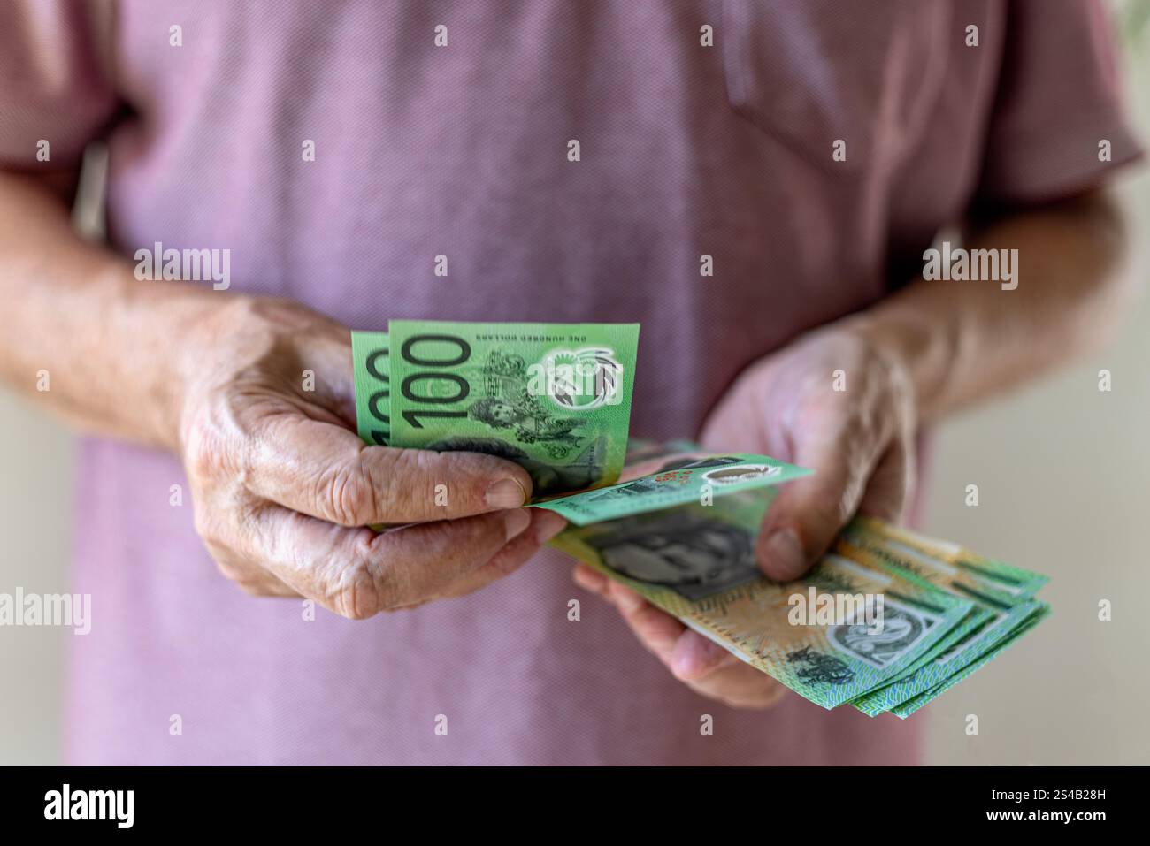 Primo piano frontale di un uomo che conta 100 banconote in dollari australiani. Concetto di denaro contante: Salari, pagamenti, dividendi, investimenti, prestiti o vincite. Foto Stock