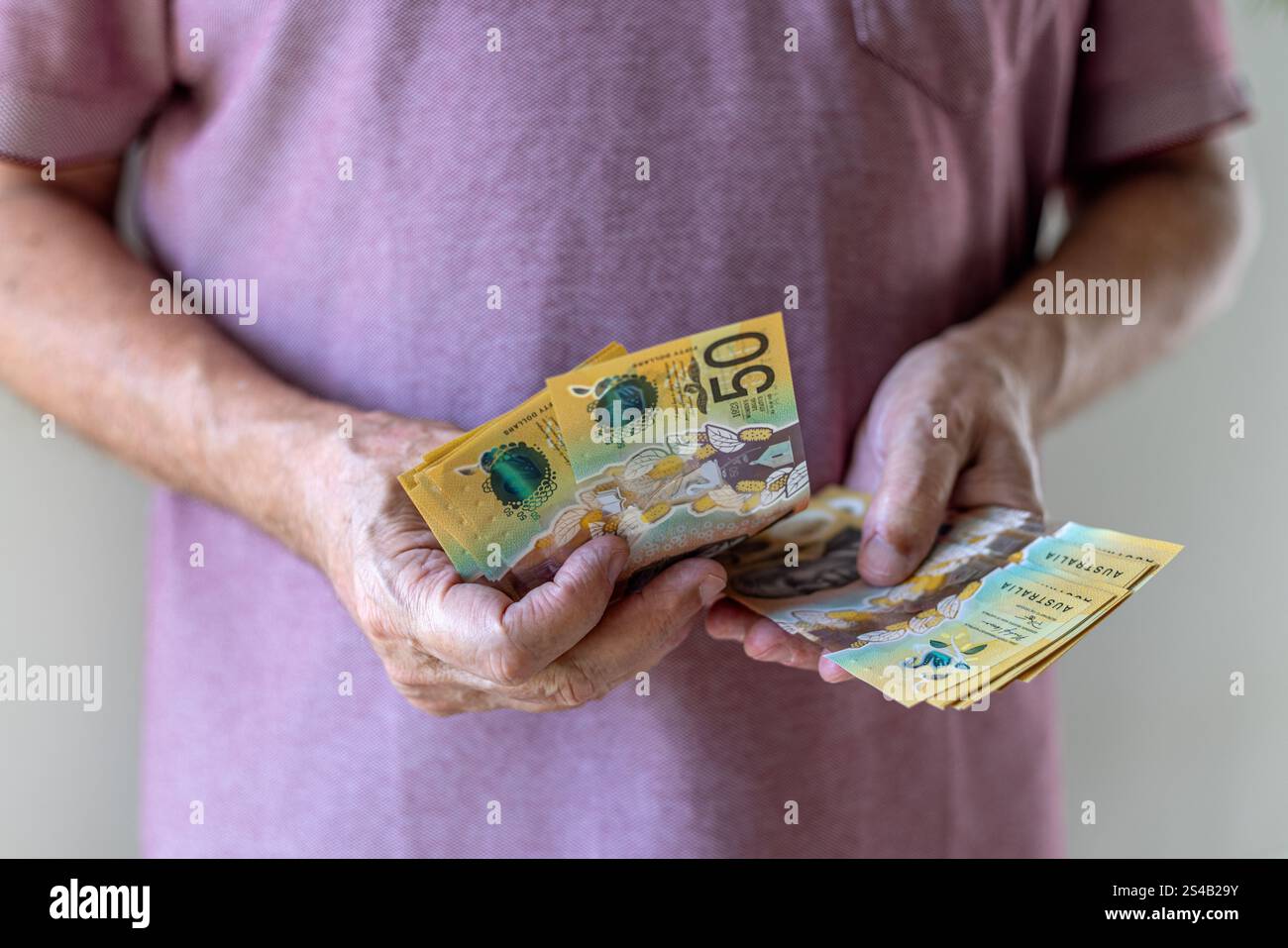 Primo piano frontale di un uomo che conta 50 banconote in dollari australiani. Concetto di denaro contante: Salari, pagamenti, dividendi, investimenti, prestiti o vincite. Foto Stock
