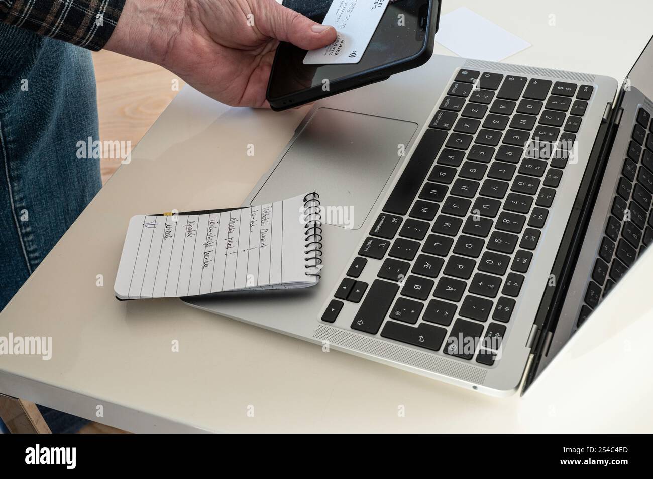 un uomo siede a un tavolo con un portatile e paga con un biglietto Foto Stock