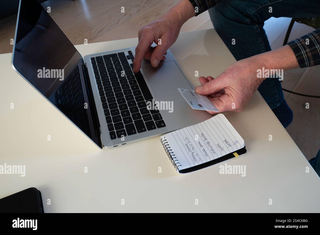 uomo a un tavolo che paga con una carta di credito sul computer Foto Stock