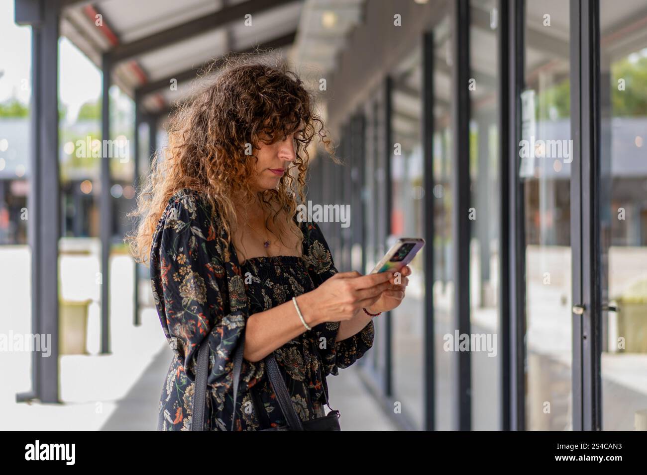 Donna alla moda che usa il suo smartphone mentre passeggia in un moderno quartiere dello shopping Foto Stock