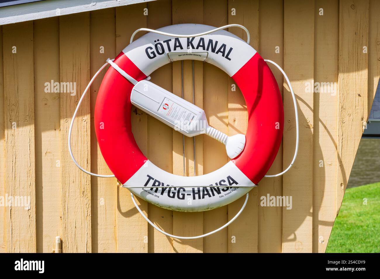 Un salvagente rosso e bianco appeso sul lato di uno stand di legno in una serratura sul canale di Göta, etichettato con il marchio della compagnia assicurativa Trygg-Hansa. Foto Stock