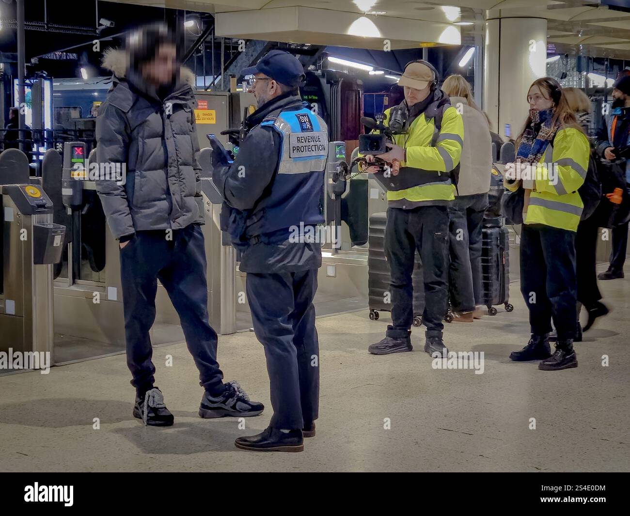 Un sospetto evasore ferroviario (L) si trova di fronte al personale addetto alla protezione delle entrate ferroviarie con un equipaggio di documentari televisivi che copre il presunto incidente a Waterloo. Foto Stock