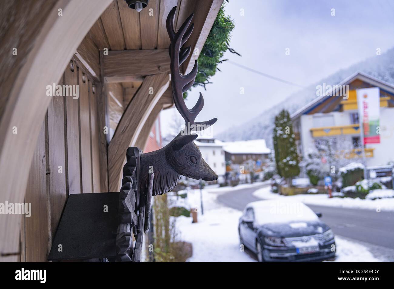 Scultura in legno di un cervo con vista su una strada innevata e automobili, Enzkloesterle, quartiere Calw, Foresta Nera, Germania, Europa Foto Stock