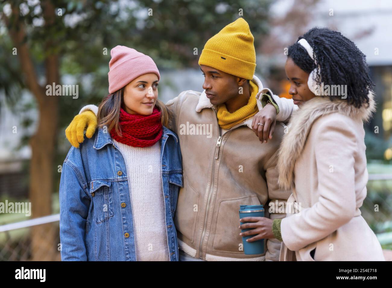 Gruppo di allegri amici multietnici che indossano abiti invernali, camminano insieme in una fredda giornata invernale, divertendosi e chiacchierando Foto Stock
