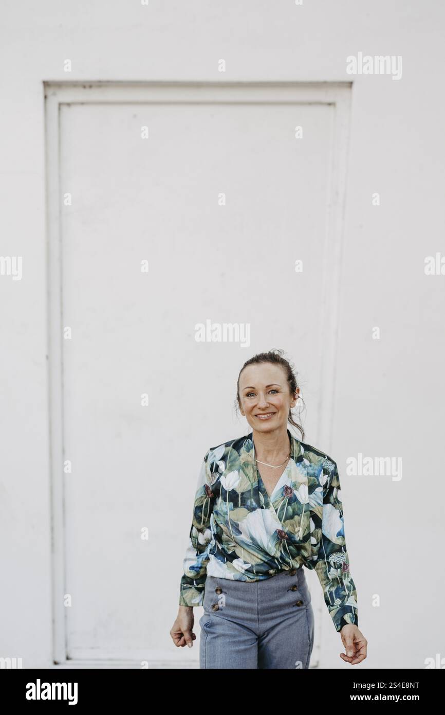Donna, più di 40 anni, in camicetta a fantasia verde davanti al muro bianco Foto Stock