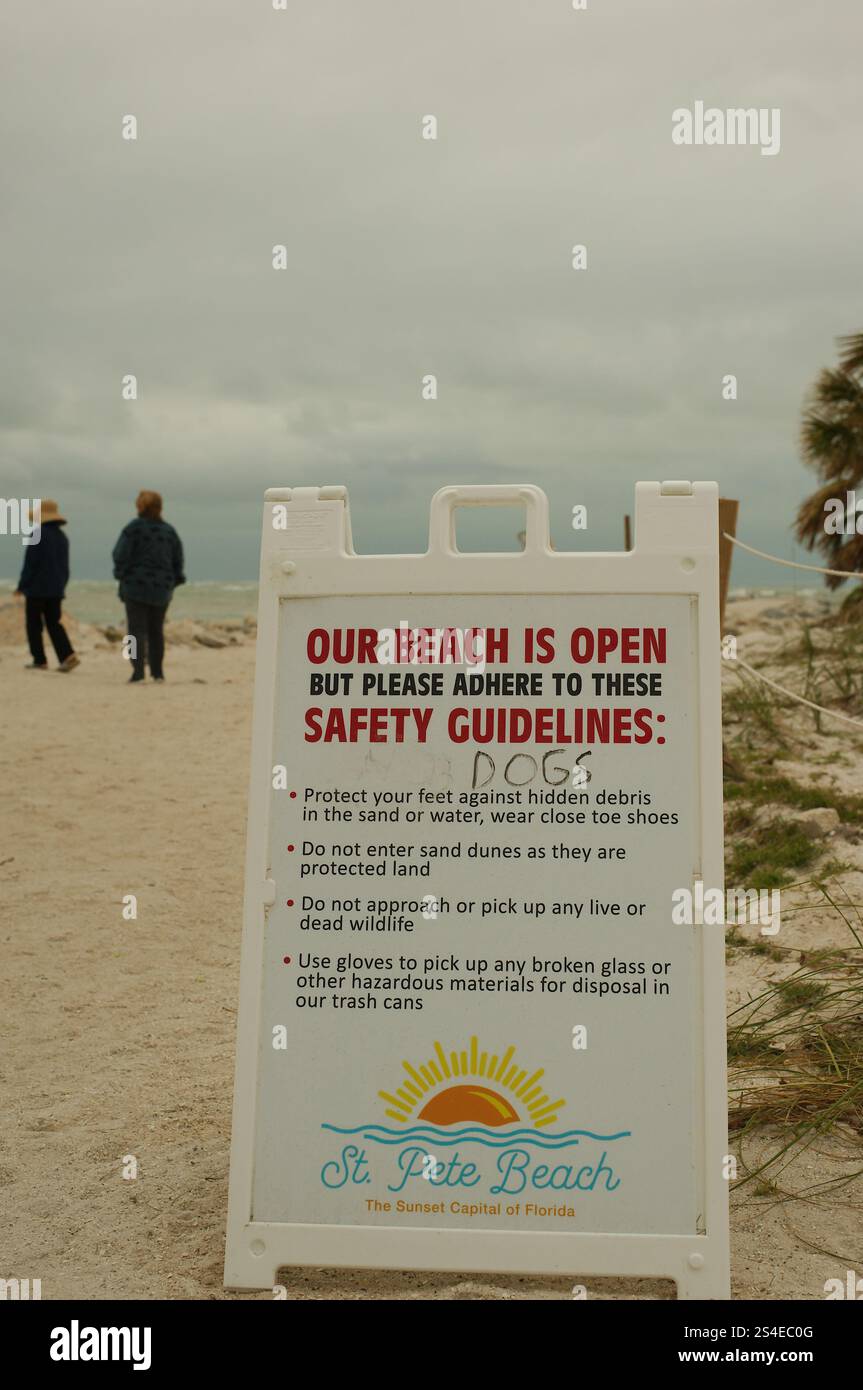 Solo per uso editoriale 12 gennaio 2025 St. Pete Beach, Florida, Stati Uniti. Cartello di avvertimento bianco A Frame all'ingresso della spiaggia. Spiaggia sabbiosa e gente nelle vicinanze Foto Stock
