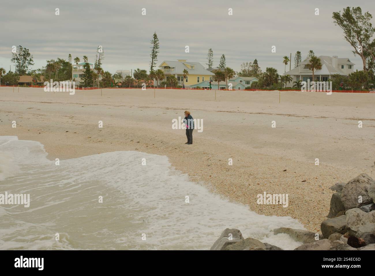 Vista diagonale sulle grandi rocce di St. Pete Beach, Florida, con una donna in giacca su sabbia. Pass-a-Grille. Onde bianche che si riversano su e stufa Foto Stock