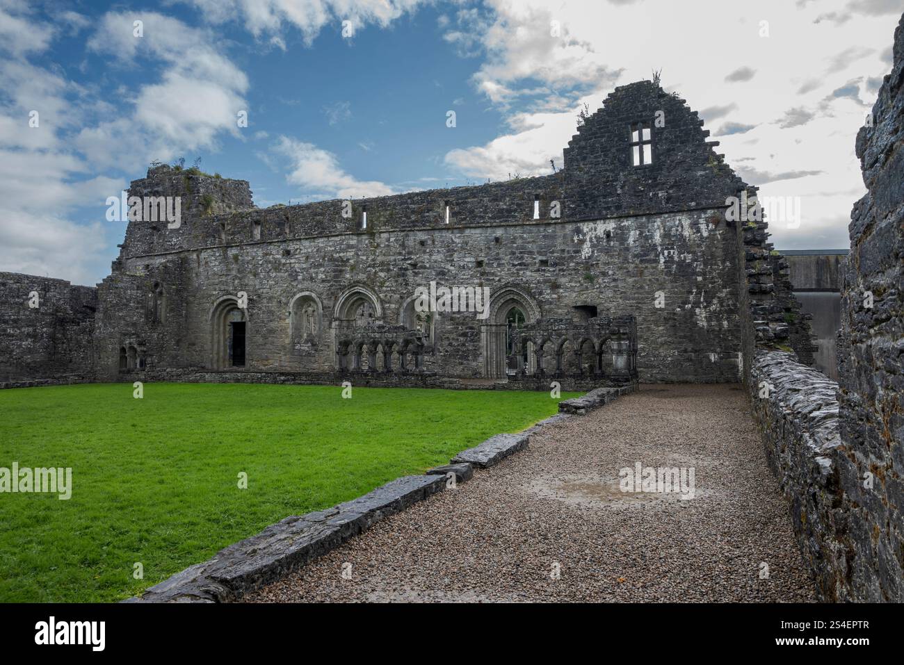 Rovine di un vecchio edificio in pietra con finestre ad arco ad Abbey Cong, Irlanda, circondato da un prato sotto un cielo parzialmente nuvoloso Foto Stock