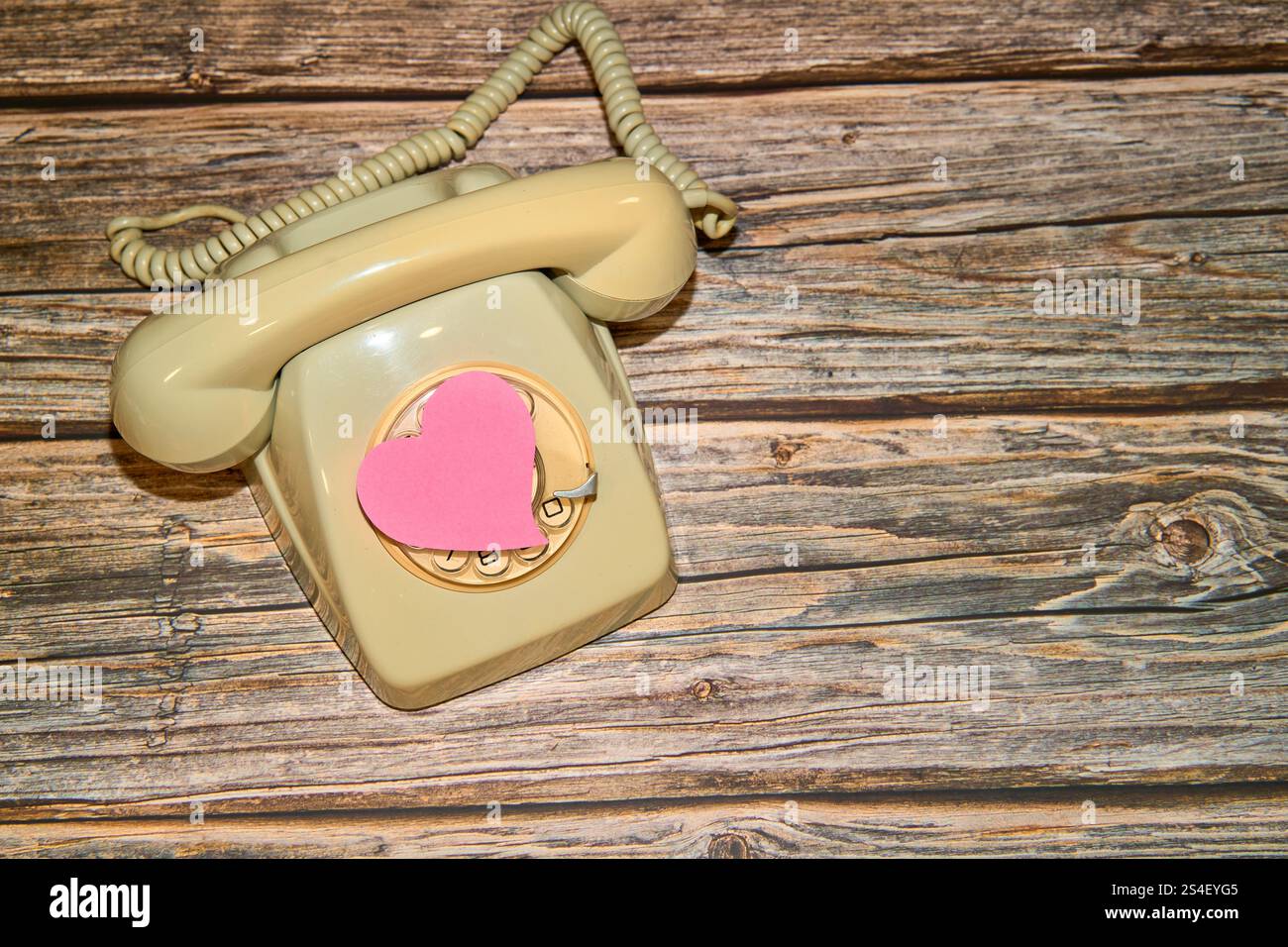 Telefono retro con cuore rosa su tavolo in legno Foto Stock