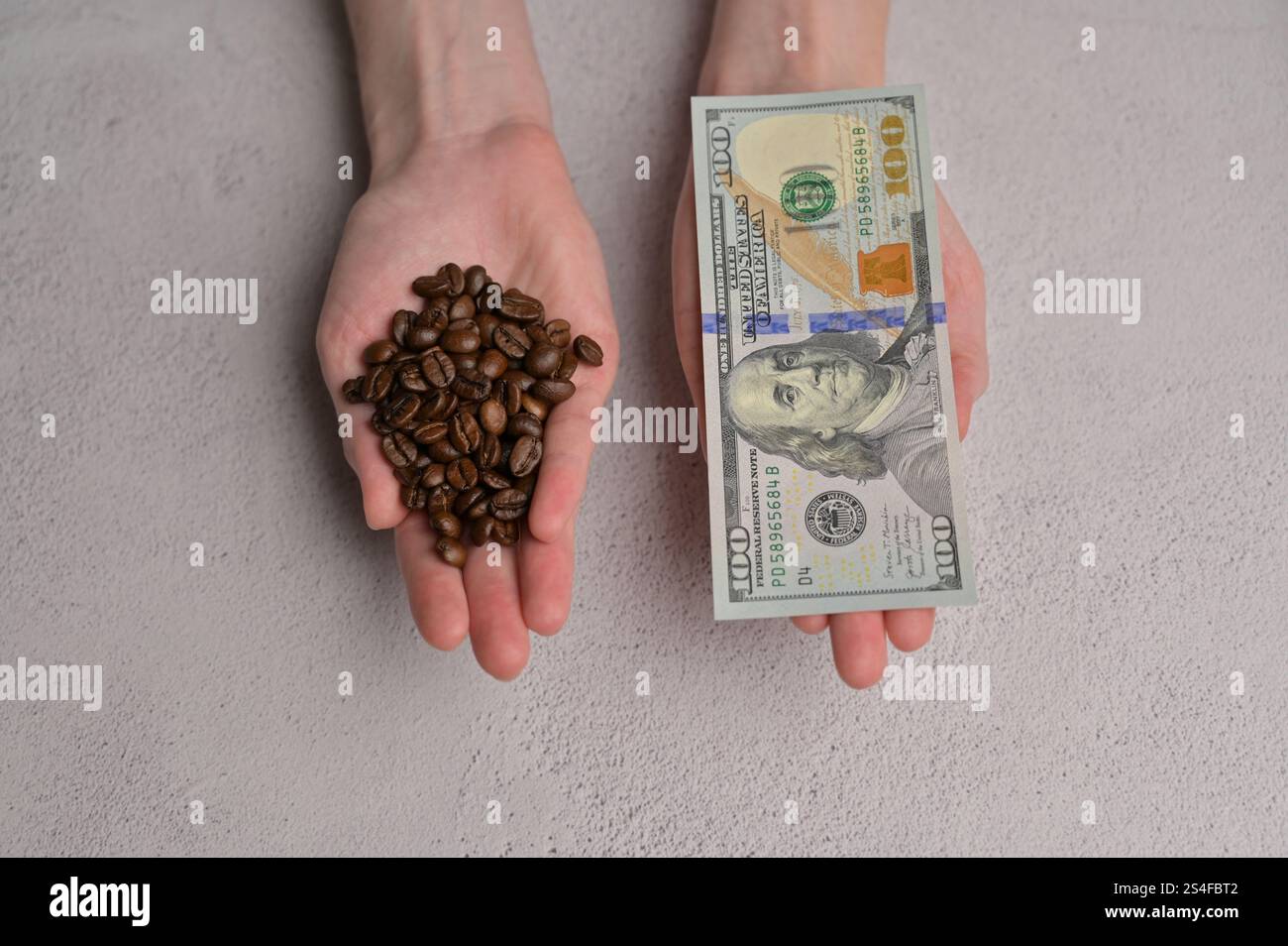 Vista dall'alto, caffè fresco con grano aromatico e banconota da 100 dollari americani in carta in contanti nelle mani di una donna, sfondo bianco. Aumento dei prezzi del caffè Foto Stock