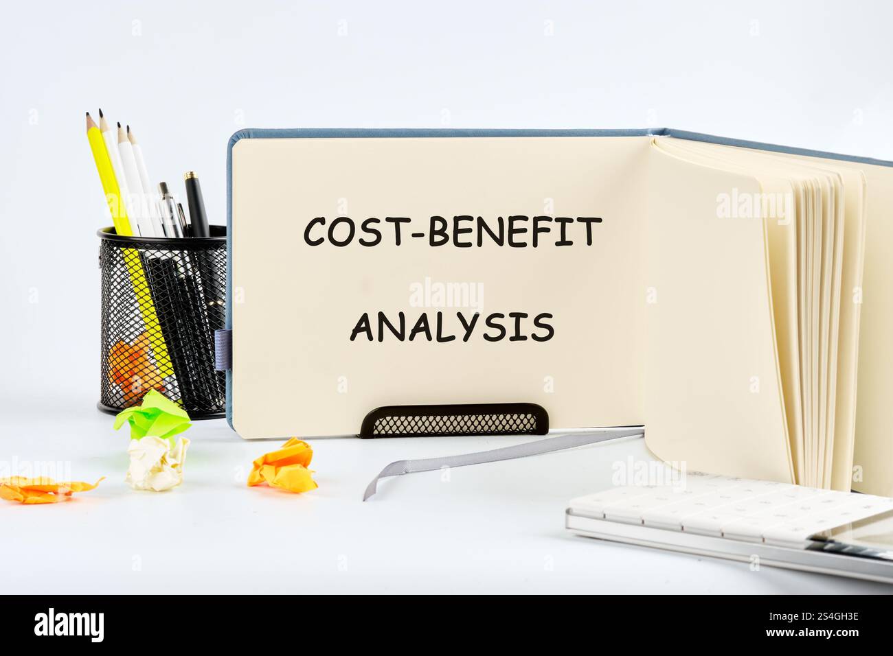 Un notebook aperto sulla pagina denominata analisi costi/benefici si trova su una scrivania accanto alla cancelleria, indicando i preparativi per una valutazione aziendale o. Foto Stock