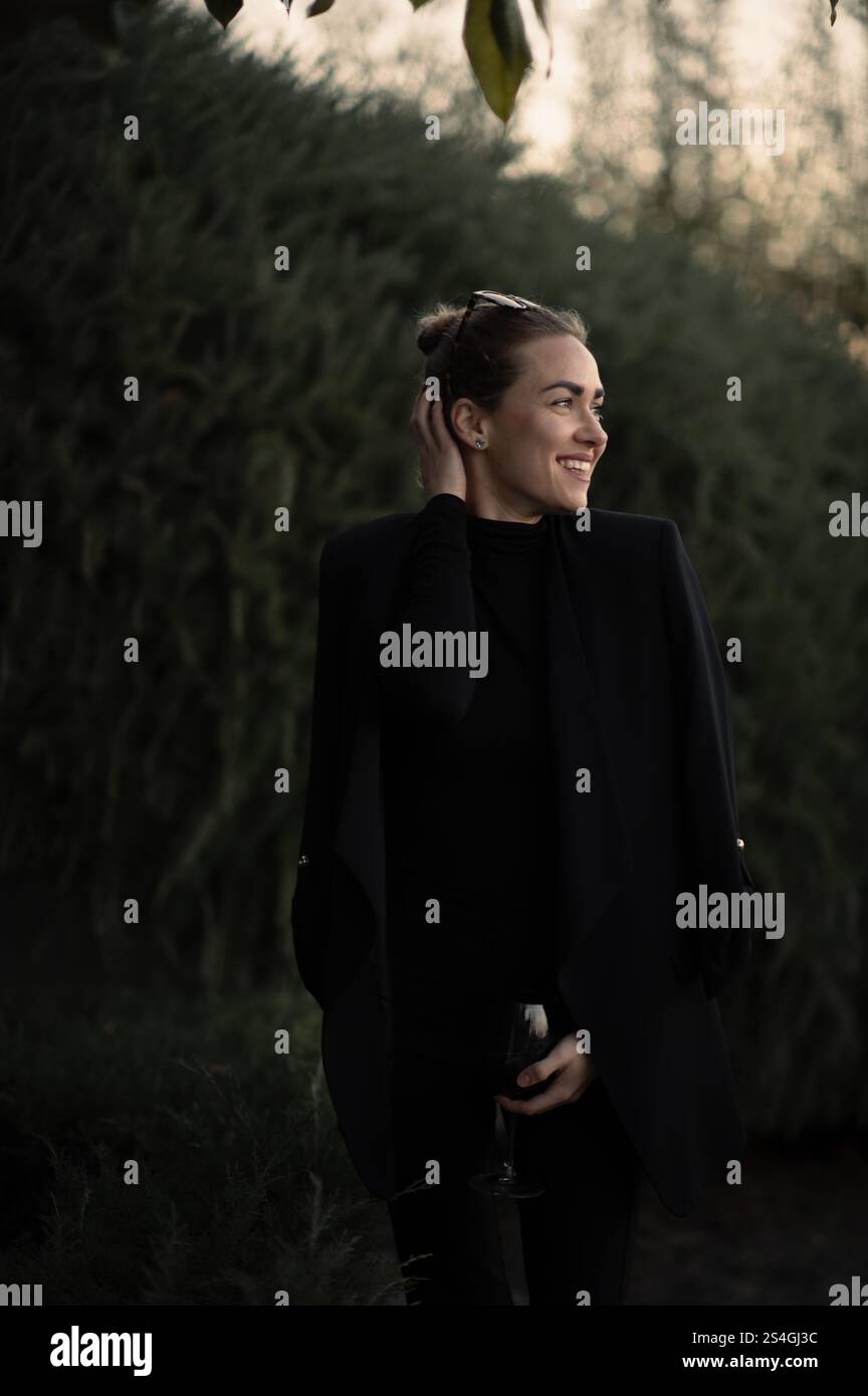 Ragazza con un bicchiere di vite a una festa sul retro in abito nero Foto Stock