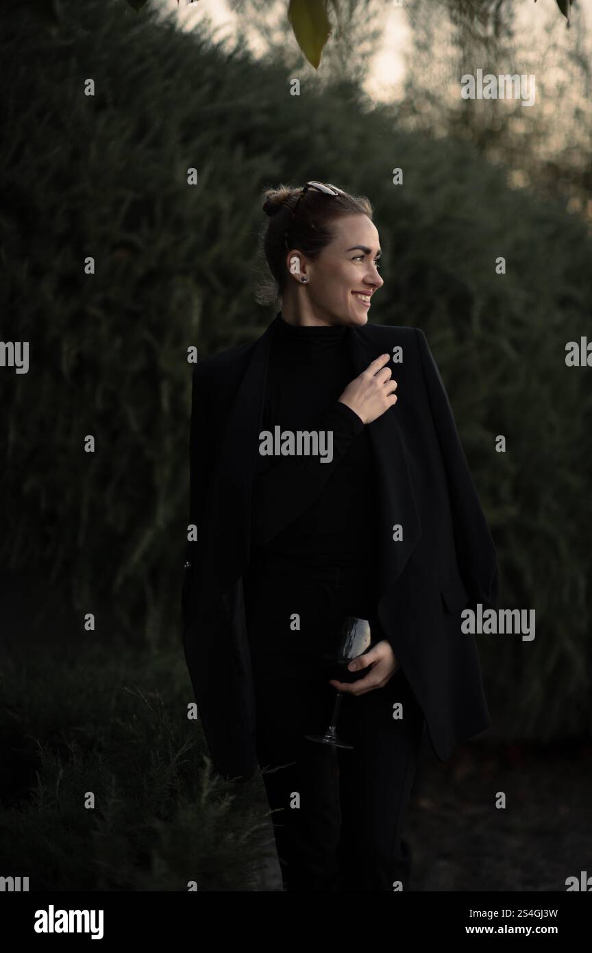 Ragazza con un bicchiere di vite a una festa sul retro in abito nero Foto Stock