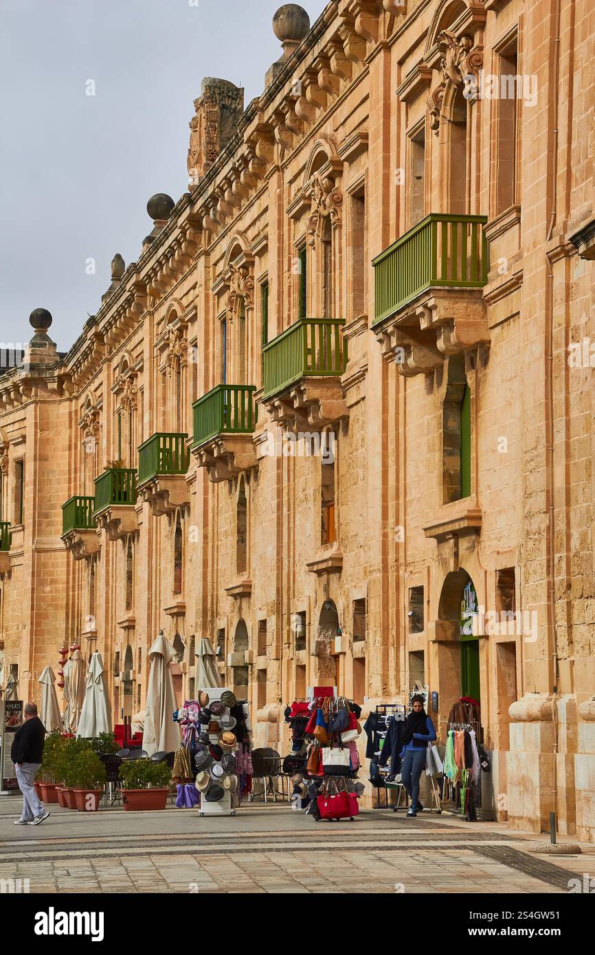 Edificio storico in pietra con balconi verdi e mercato all'aperto a Valletta, Malta. Foto Stock