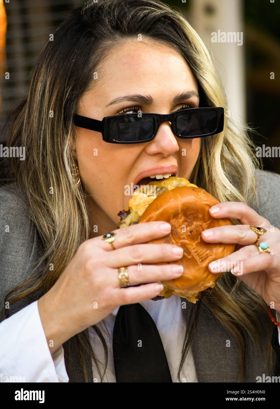Una giovane donna d'affari che mangia un hamburger in un bar all'aperto Foto Stock