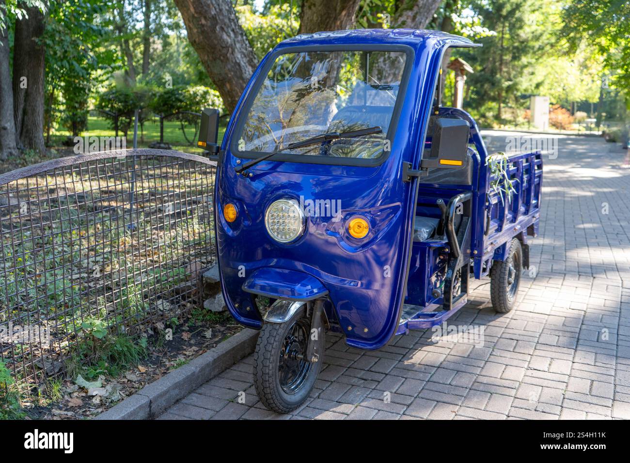 Motocicletta a tre ruote con cabina. Piccola auto blu con rimorchio per uno. Trasporto intelligente. Triciclo elettrico per il carico. Foto Stock