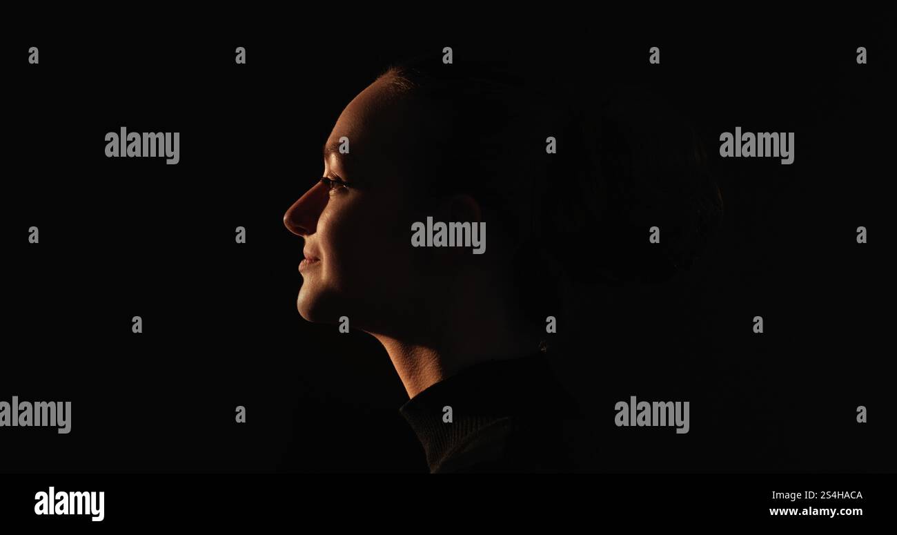 Faccia pacifica. Silhouette ispirata. Tranquillità interiore. Profilo scuro di una donna felice che sorride isolato su sfondo nero. Foto Stock