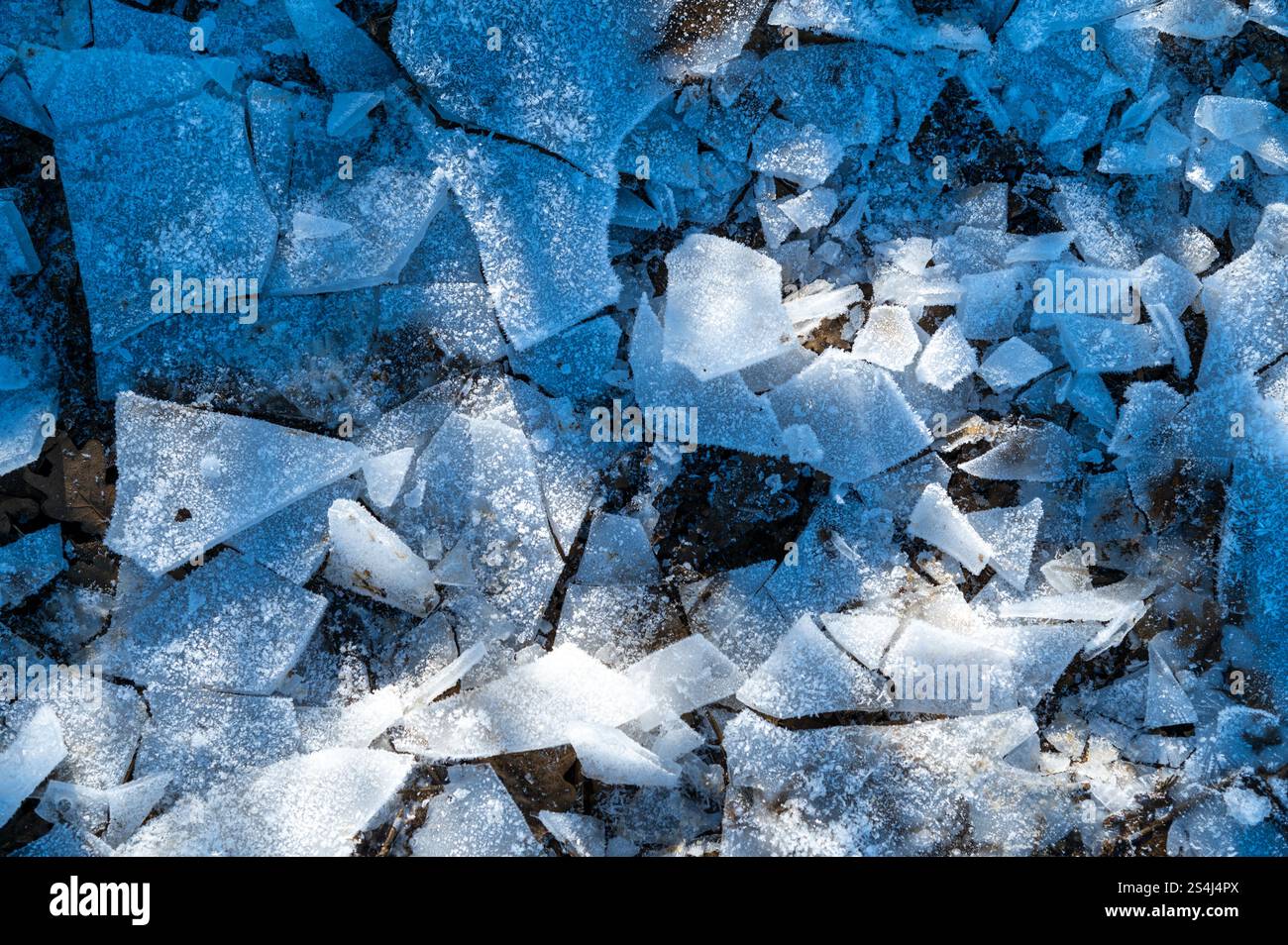 Il ghiaccio rotto e smerigliato si frammenta su una pozza ghiacciata, illuminata dalla bassa luce solare invernale, creando un'atmosfera invernale strutturata Foto Stock