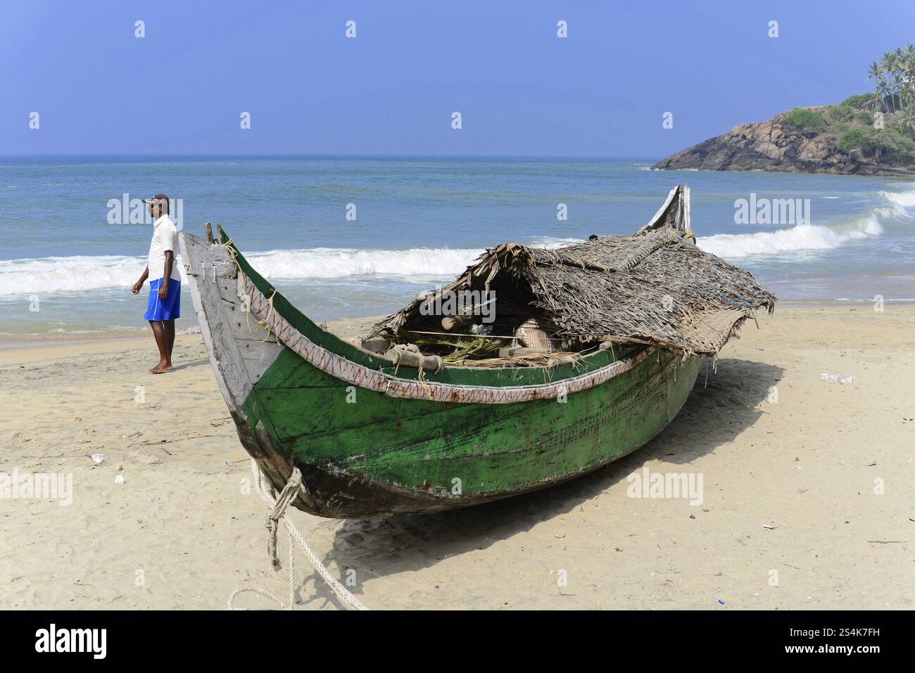 Kovalam Beach, Malabar Coast, Malabar, Kerala, India meridionale, India, Asia, Una barca tradizionale sulla spiaggia, un uomo in piedi accanto ad essa, onde calme nel Foto Stock