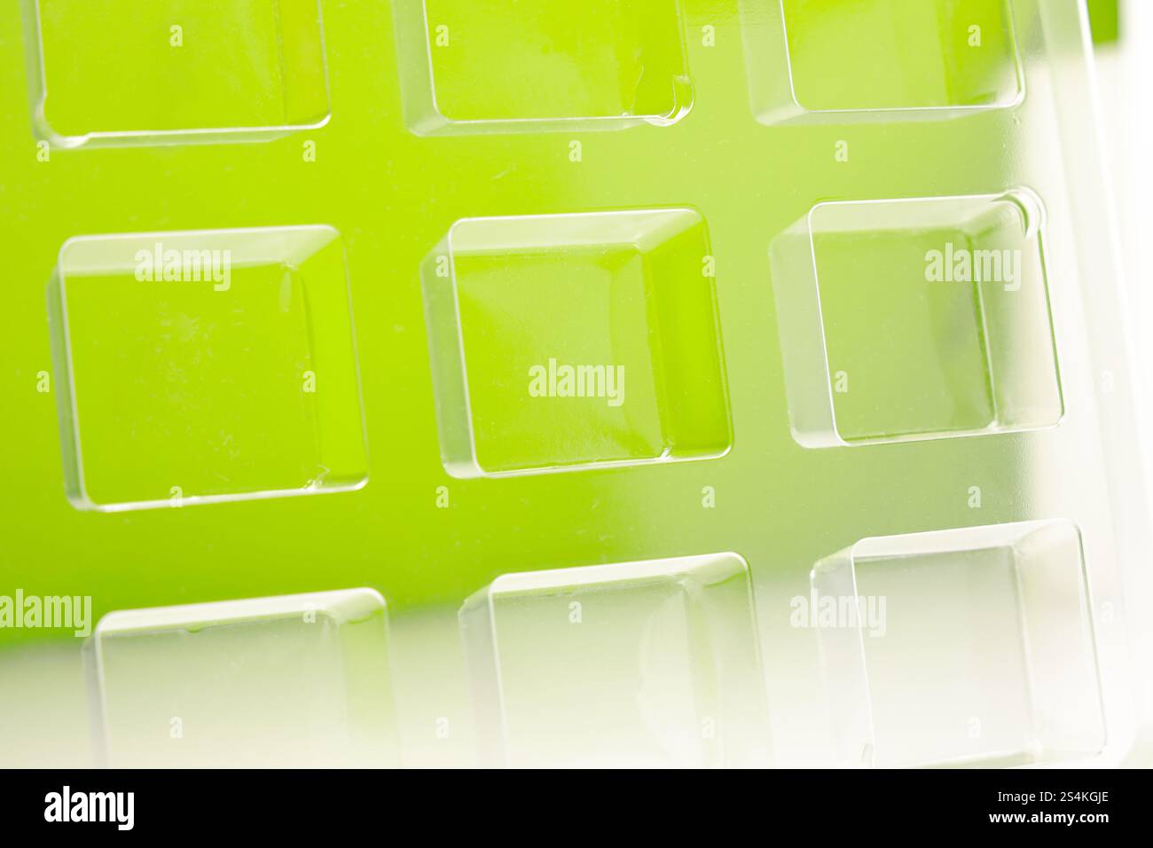 Uno stampo per termoformatura quadrato trasparente industriale realizzato in plastica come soluzione di imballaggio per prodotti industriali. Vassoio in alluminio su sfondo verde. Foto Stock