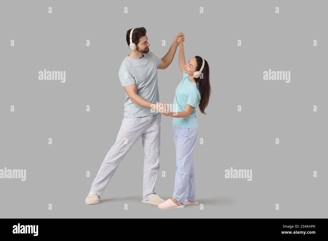 Coppia innamorata in pigiama con cuffie che ballano su sfondo chiaro Foto Stock