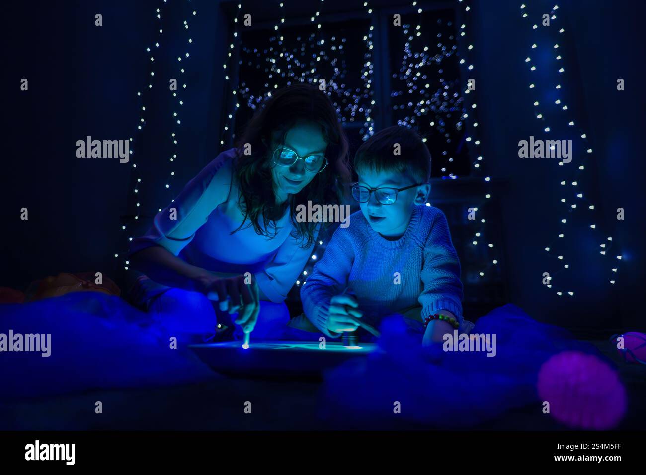 Bambino e terapista in camera stimolante sensoriale, Black snoezelen. Bambino autistico che gioca con il terapista durante la sessione di terapia occupazionale. Foto Stock