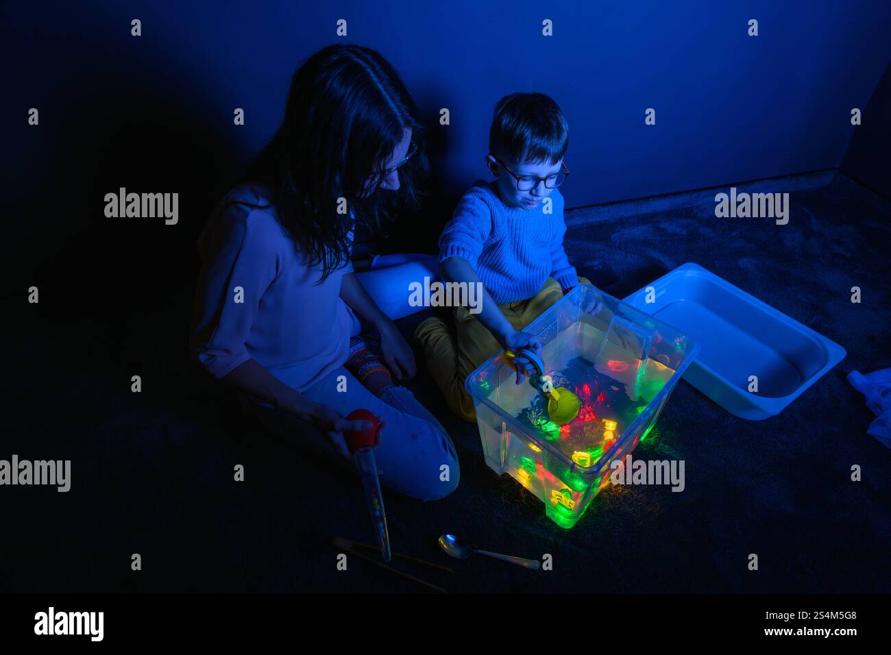 Bambino e terapista in camera stimolante sensoriale, Black snoezelen. Bambino autistico che gioca con il terapista durante la sessione di terapia occupazionale. Foto Stock