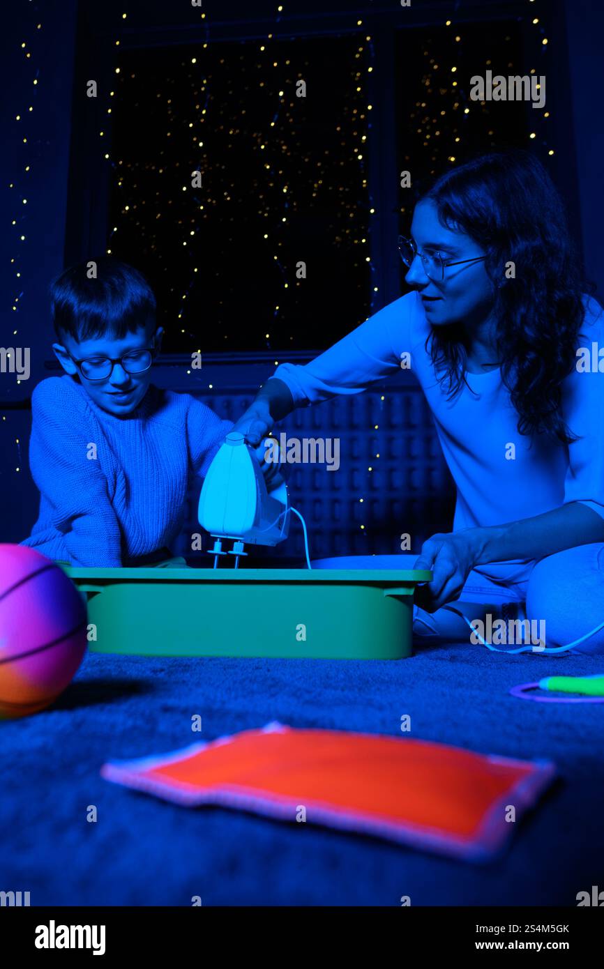 Bambino e terapista in camera stimolante sensoriale, Black snoezelen. Bambino autistico che gioca con il terapista durante la sessione di terapia occupazionale. Foto Stock