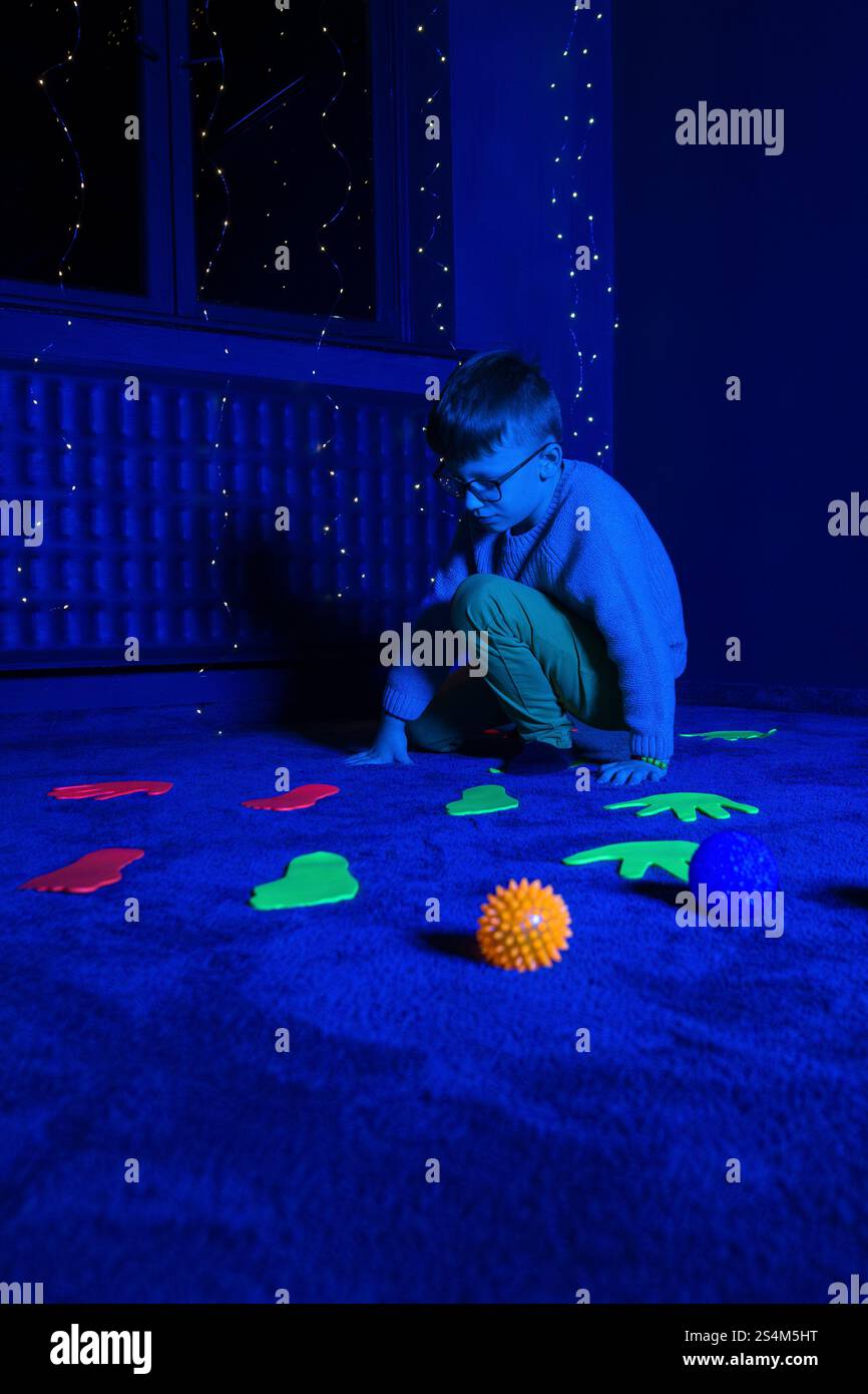Bambino in sala terapia stimolante sensoriale, nero snoezelen. Bambino autistico che gioca durante la sessione di terapia. Terapia occupazionale. Stimolo sensoriale terapeutico Foto Stock