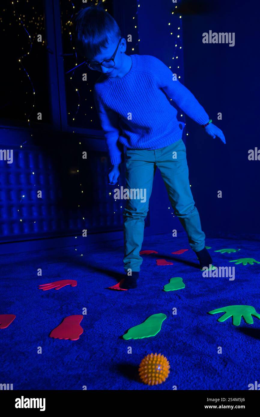 Bambino in sala terapia stimolante sensoriale, nero snoezelen. Bambino autistico che gioca durante la sessione di terapia. Terapia occupazionale. Stimolo sensoriale terapeutico Foto Stock
