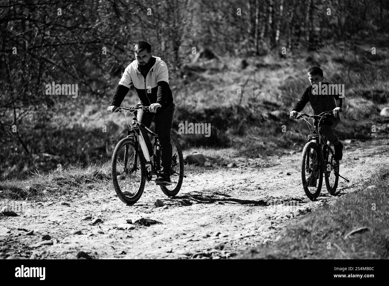 Un'impressionante immagine in bianco e nero cattura un padre e un figlio in bicicletta insieme su un sentiero polveroso. Viaggiano fianco a fianco, godendosi un'esperienza condivisa. Foto Stock
