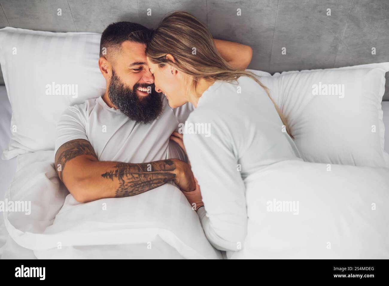 La mattina, una giovane coppia felice e amorevole è sdraiata a letto. Sono rilassanti e sorridenti. Foto Stock