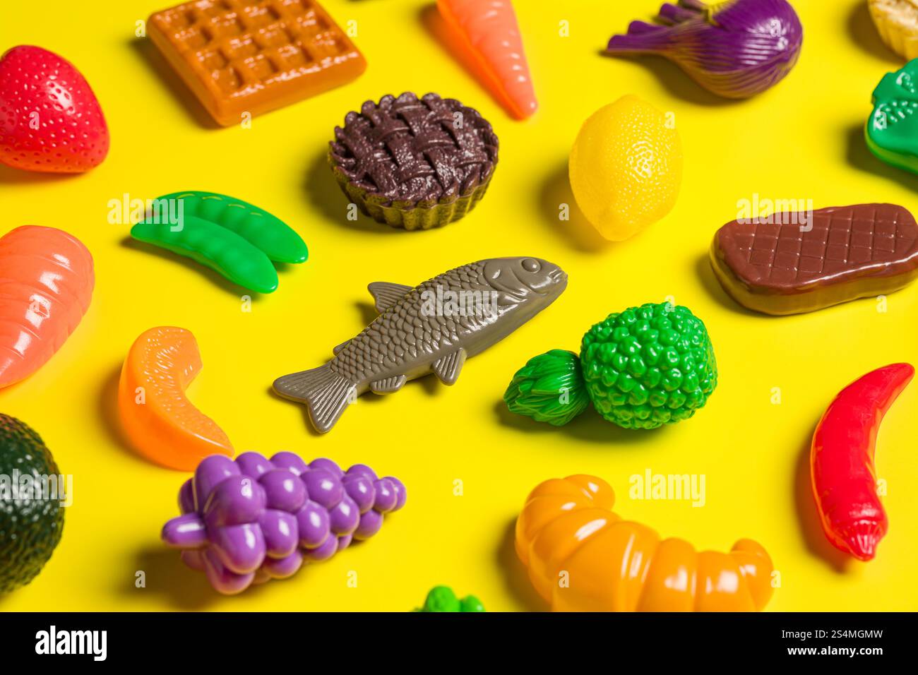 Una vivace collezione di coloratissimi modelli di cibo in plastica su sfondo giallo raffigura la critica del cibo spazzatura e della cultura dietetica, mettendo in risalto arti Foto Stock