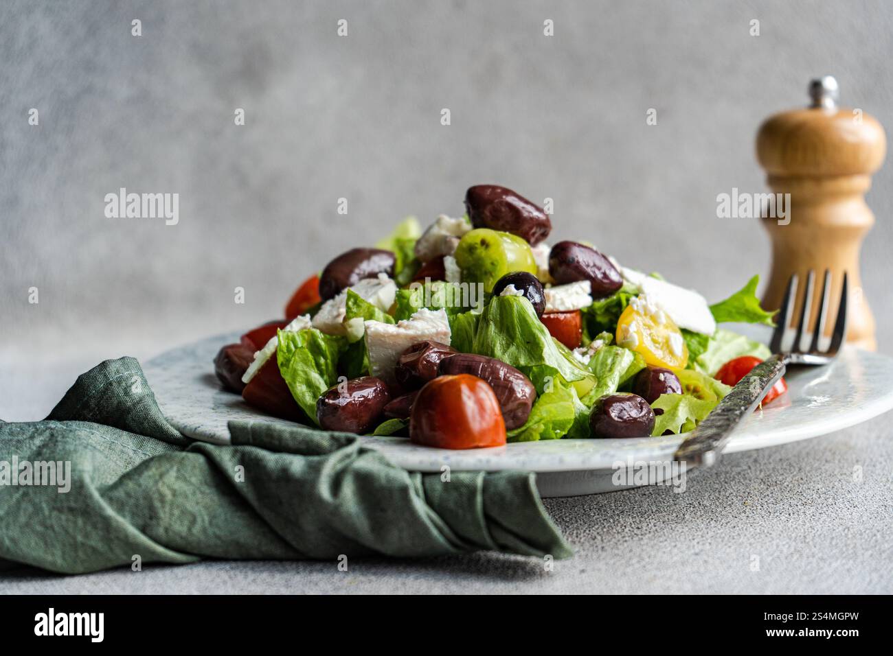 Una vivace insalata greca con pomodori, lattuga e olive rosse, condita con formaggio feta e olio d'oliva accompagnati da uno shaker di pepe Foto Stock