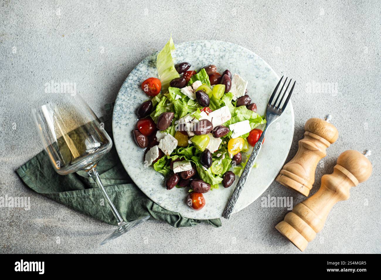 Una vivace insalata greca con pomodori succosi, lattuga croccante, feta e olive rosse, abbinata a un bicchiere di vino bianco freddo su un tavolo rustico Foto Stock
