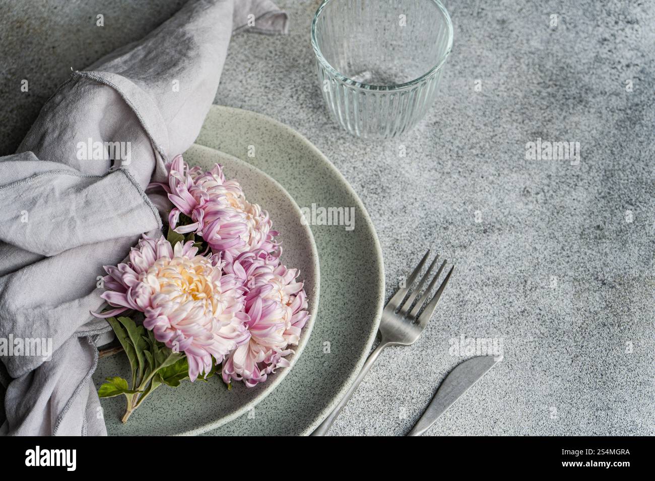 Un ambiente rustico e morbido presenta crisantemi rosa e crema su piatti in ceramica con tovagliolo di lino. L'accogliente tema autunnale aggiunge calore a questo ristorante Foto Stock