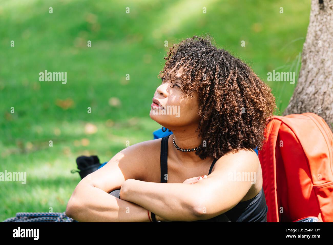 Una donna Nera siede sotto un albero in un parco di Bogotà, riposando le braccia sulle ginocchia mentre guarda in lontananza circondata dal verde, appare Ref Foto Stock