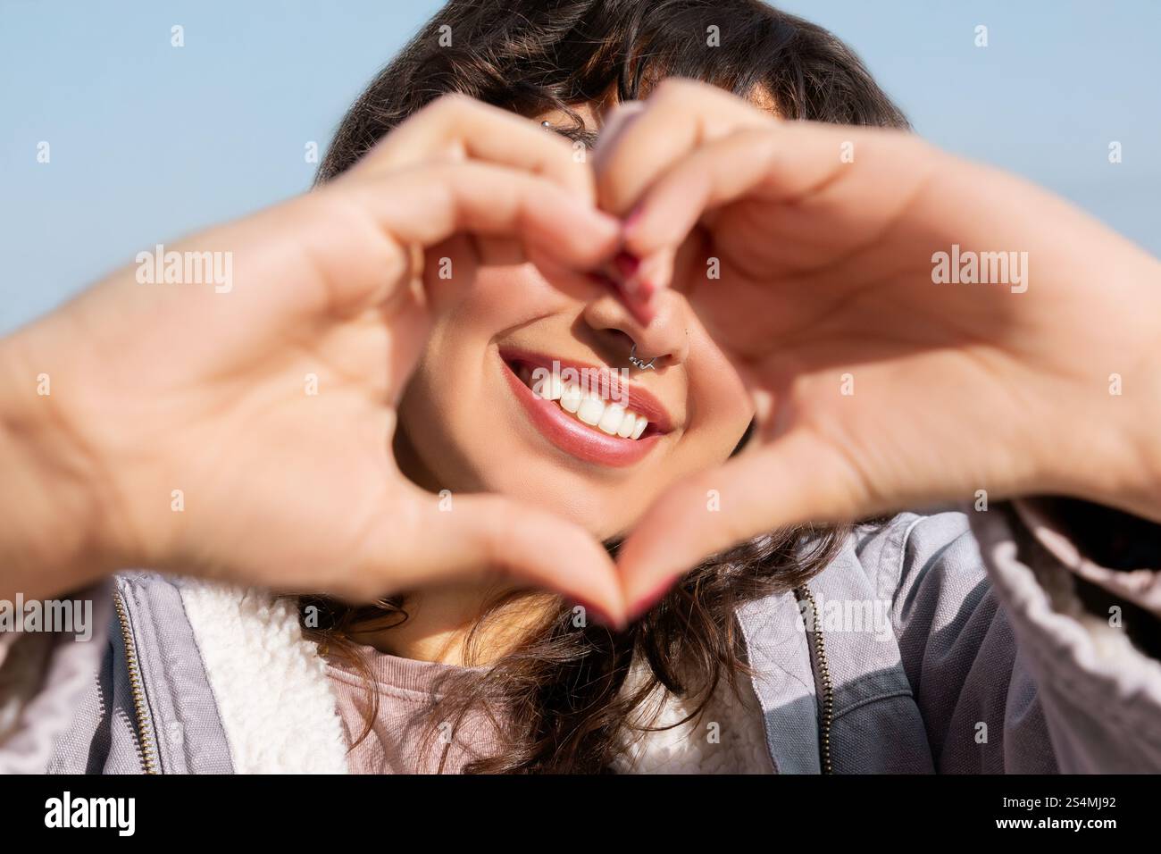 Una giovane donna allegra con i capelli scuri forma il cuore con le mani, mostrando la sua energia positiva e il suo spirito spensierato, perfetti per lo stile di vita e. Foto Stock