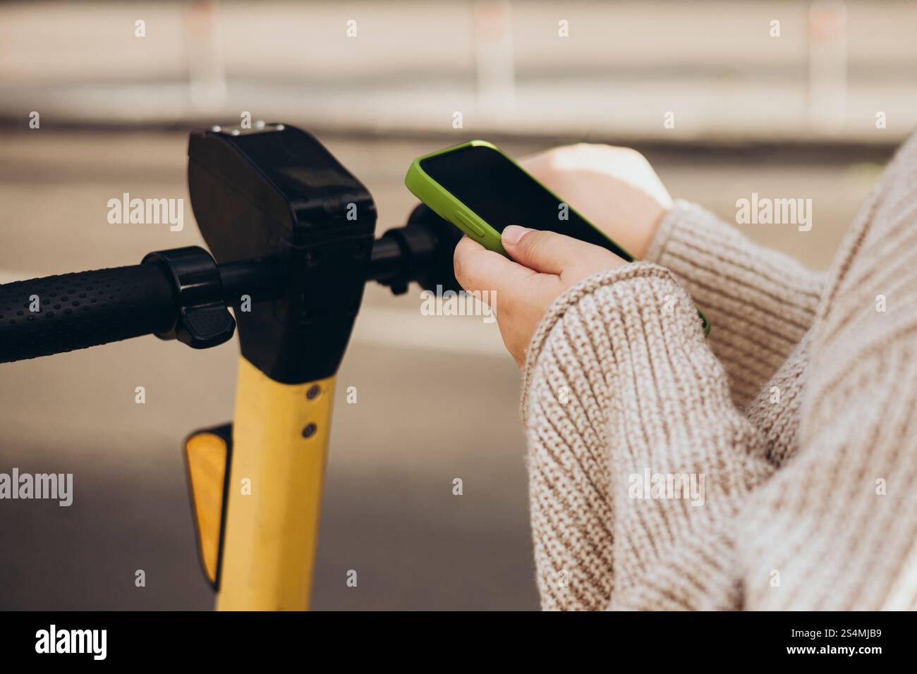 Una donna corta e irriconoscibile scansiona il codice QR con uno smartphone per noleggiare uno scooter elettrico. L'attenzione e' sulle sue mani tenendo sia il telefono che lo scooter Foto Stock