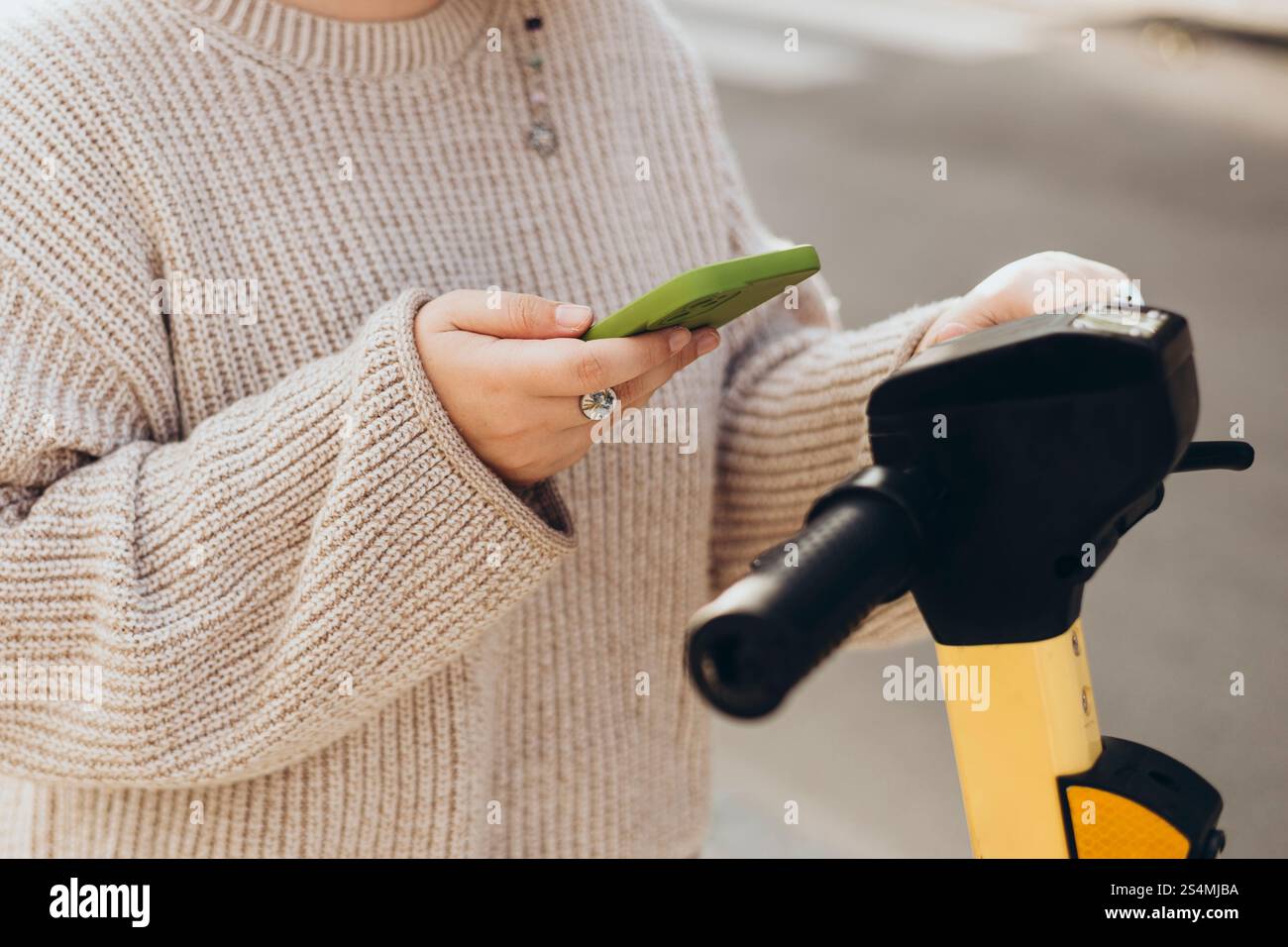 Una donna corta e irriconoscibile scansiona il codice QR con uno smartphone per noleggiare uno scooter elettrico. L'attenzione e' sulle sue mani tenendo sia il telefono che lo scooter Foto Stock