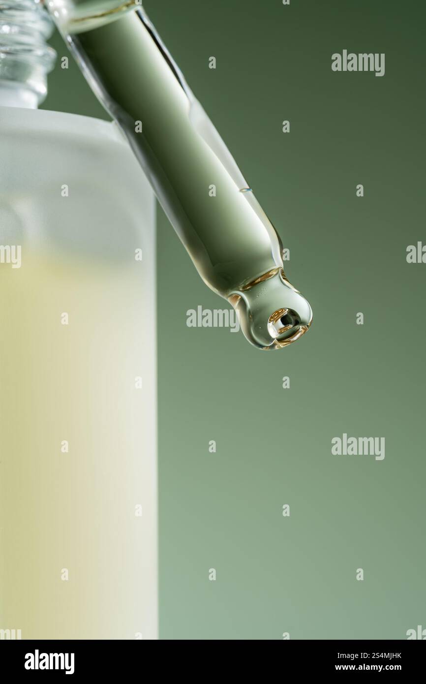 Una macro shot di un contagocce cosmetico per siero che dispensa una goccia, su uno sfondo verde tenue. Foto Stock