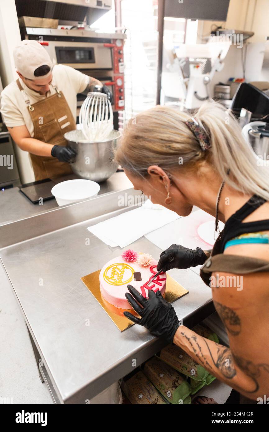 Due pasticceri progettano e preparano sapientemente una torta colorata in una panetteria italiana, una mescola la pastella, mentre l'altra decora meticolosamente, mettendo in mostra Foto Stock