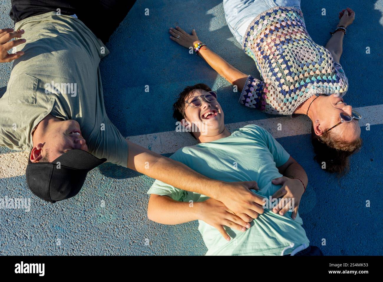 Un adolescente con sindrome di Down gode di una giornata di sole sdraiato su un campo sportivo con la famiglia che sottolinea la gioia del tempo in famiglia e l'inclusività nello sport Foto Stock
