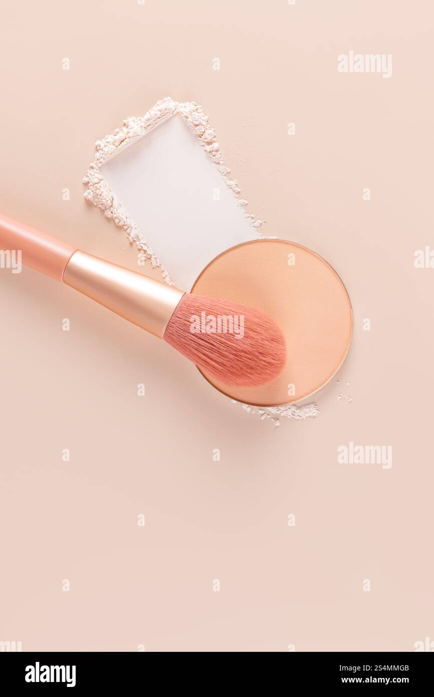 Vista dall'alto di una spazzola per il trucco e polvere compatta accanto alla polvere sciolta su una superficie beige, ideale per temi estetici e di bellezza. Foto Stock