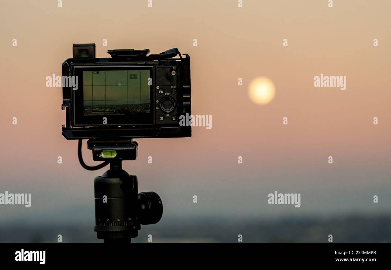 Una fotocamera professionale su un treppiede si affaccia su un tramonto tranquillo, pronto a catturare il momento perfetto. Foto Stock
