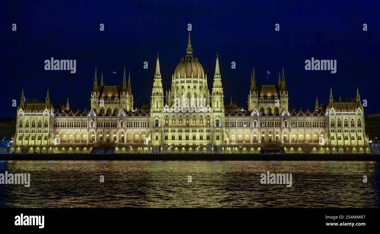 L'edificio del Parlamento ungherese, illuminato di notte, riflette la sua grandezza sulle acque del Danubio. Foto Stock