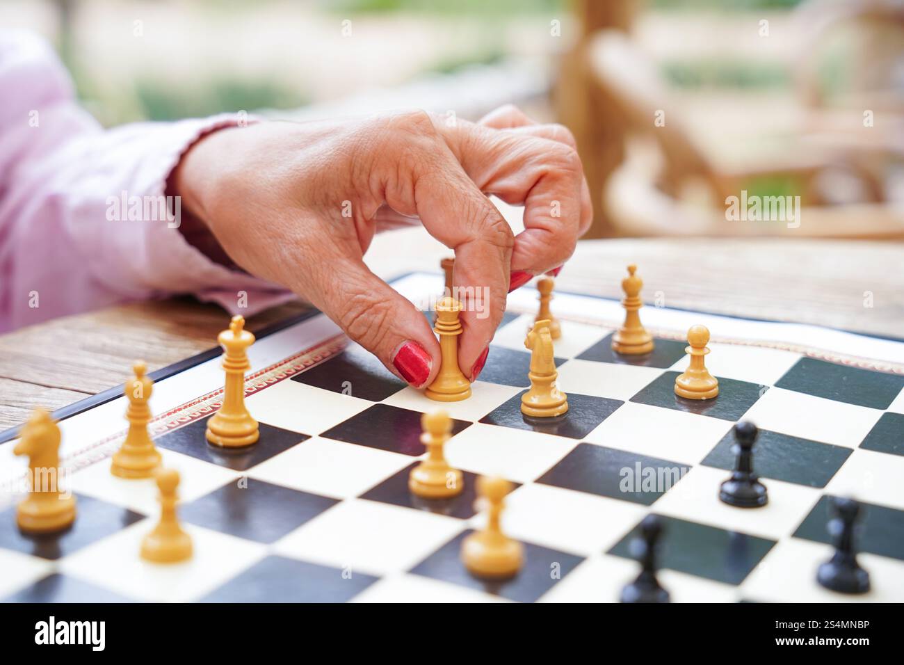 Una mano sposta strategicamente un pezzo di scacchi su una tavola durante una partita all'aperto. L'ambientazione sottolinea l'attenzione e la strategia di questo gioco classico Foto Stock